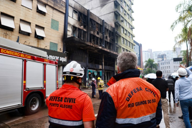 Members of civil defense stand at the site of a deadly fire at a guesthouse in Porto Alegre