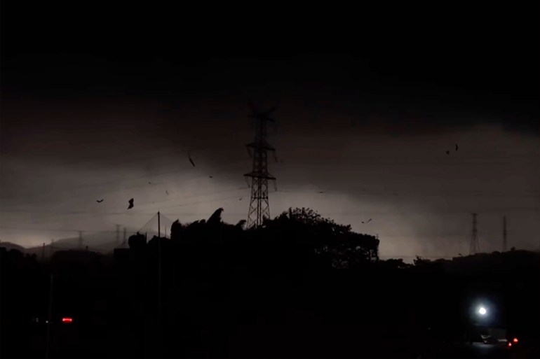 The storm over the Baiyun district. The sky is almost black and an electricity pylon is silhouetted against the lighter clouds.. There is debris being blown about by the wind.