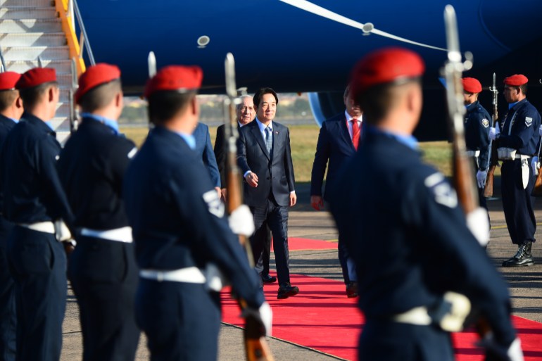 Lai walking on a red carpet as he arrives in Paraguay. An honour guard is standing to attention on one side.