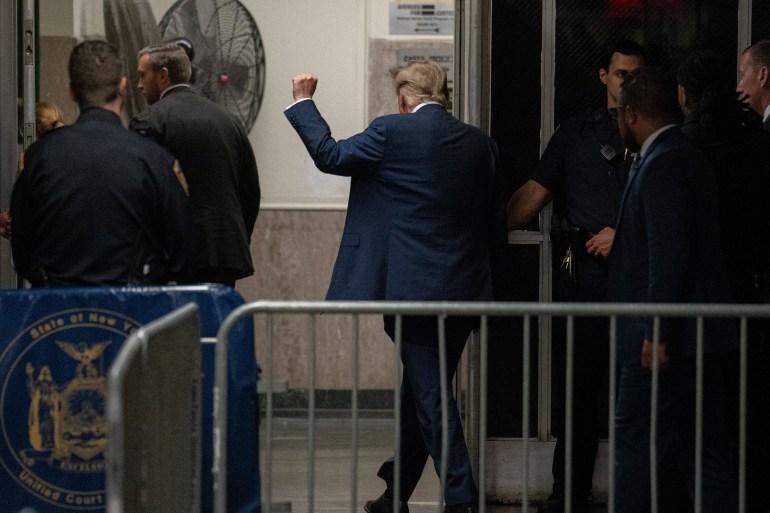 Donald Trump walks into court, behind metal barricades, with a raised fist in the air.