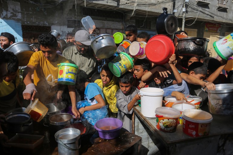 Palestinians crowd together as they wait for food distribution in Rafah, They are holding buckets and bowls.
