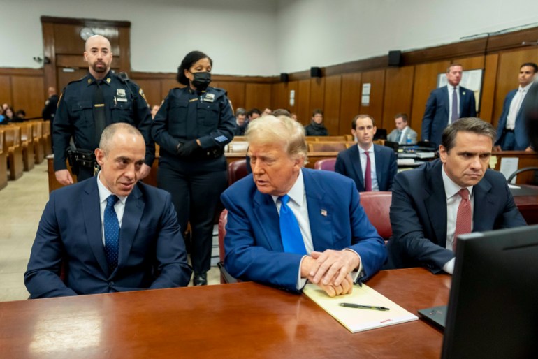 Donald Trump sits at the defence table and leans towards his lawyers in court.