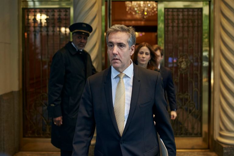 Michael Cohen exits his apartment building in New York to head to trial. He wears a yellow tie and dark suit.