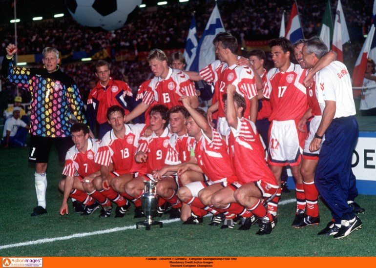 Football players stand together around trophy.