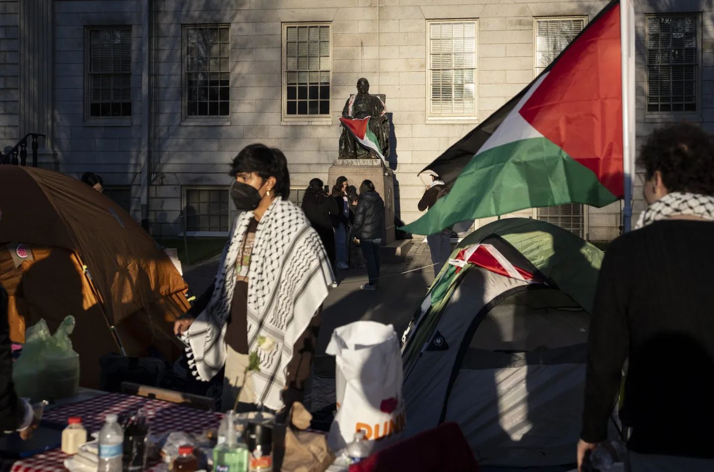 A student protester stands in front of the statue of John Harvard, the first major benefactor of Harvard College, draped in the Palestinian flag, at an encampment of students protesting against the war in Gaza, at Harvard University in Cambridge, Mass., April 25, 2024. 