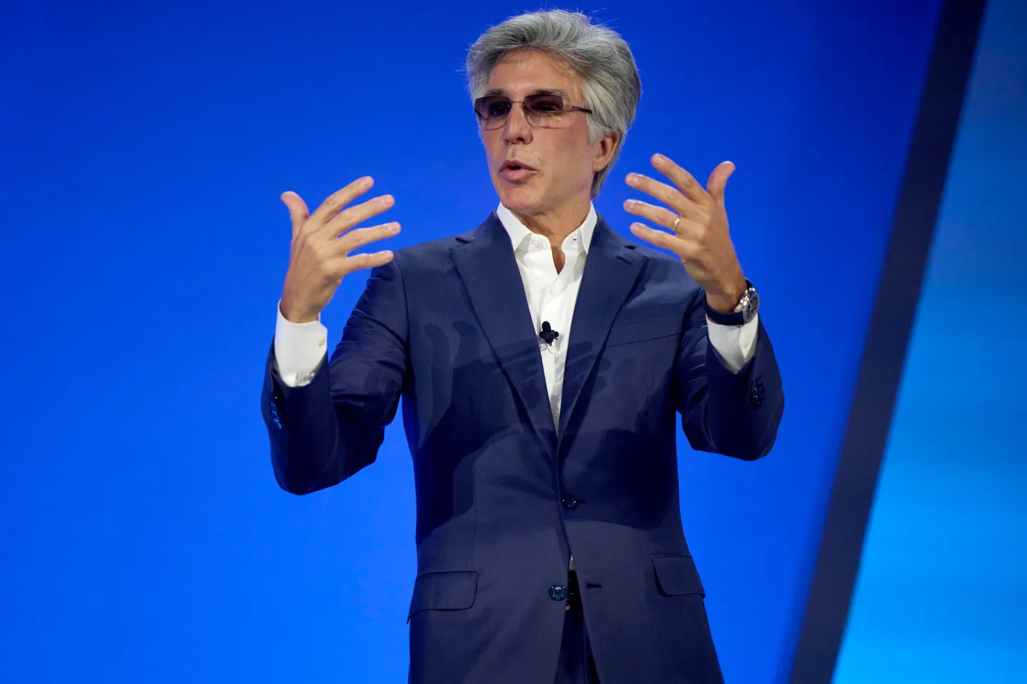 Bill McDermott, chief executive officer of ServiceNow Inc. on stage, in front of a blue background, gesturing with both hands.