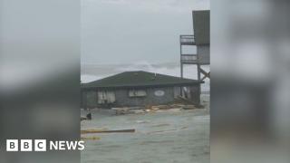 Moment houses on stilts topple into the sea